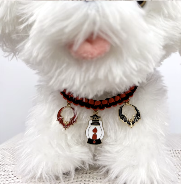 Cat wearing a Halloween breakaway collar with a small pumpkin pendant and festive woven design.