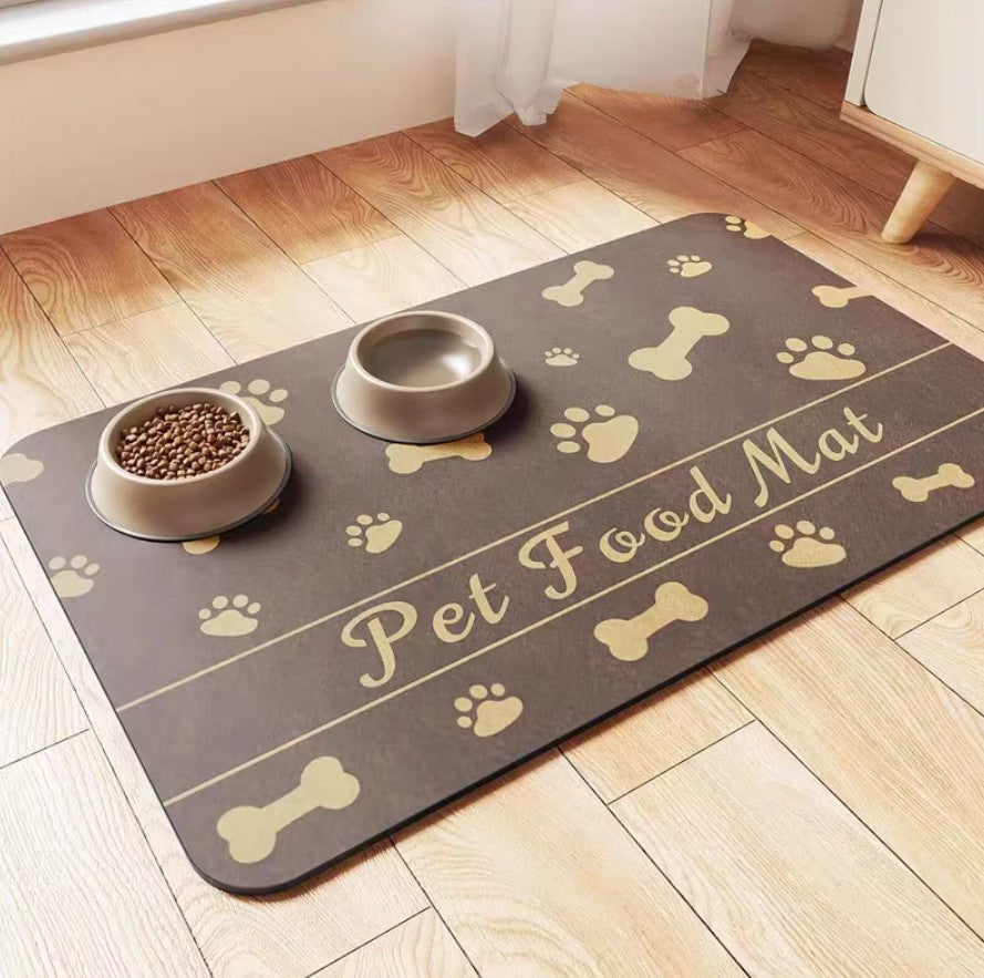 Pet feeding mat with bowls on a wooden floor, featuring bone and paw print design, ideal for cats and dogs.